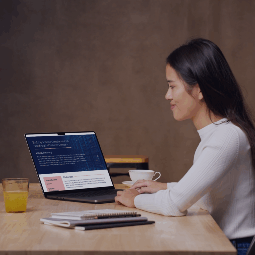 Woman reviewing a pharmaceutical QMS case study on a laptop in a modern office setting.