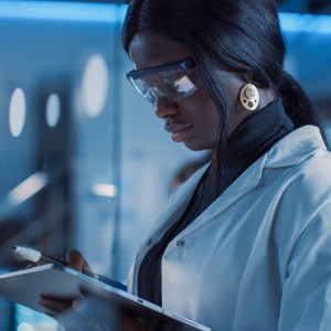 In,The,Research,Laboratory,Smart,And,Beautiful,African,American,Female In the Research Laboratory Smart and Beautiful African American Female Scientist Wearing White Coat and Protective Glasses Writes Formula on Glass Whiteboard, References Her Tablet Computer